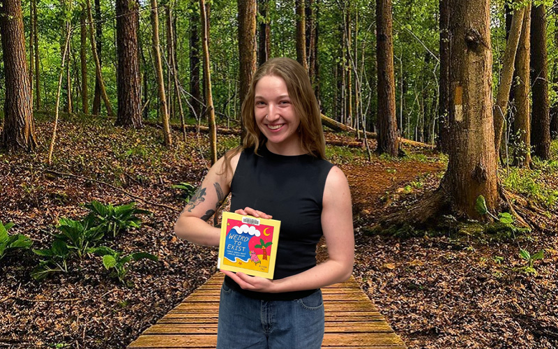 Young woman holding a book in a wooded setting.