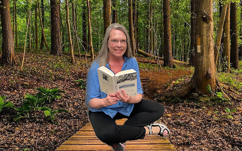 Women with an open book sitting in a wooded setting.