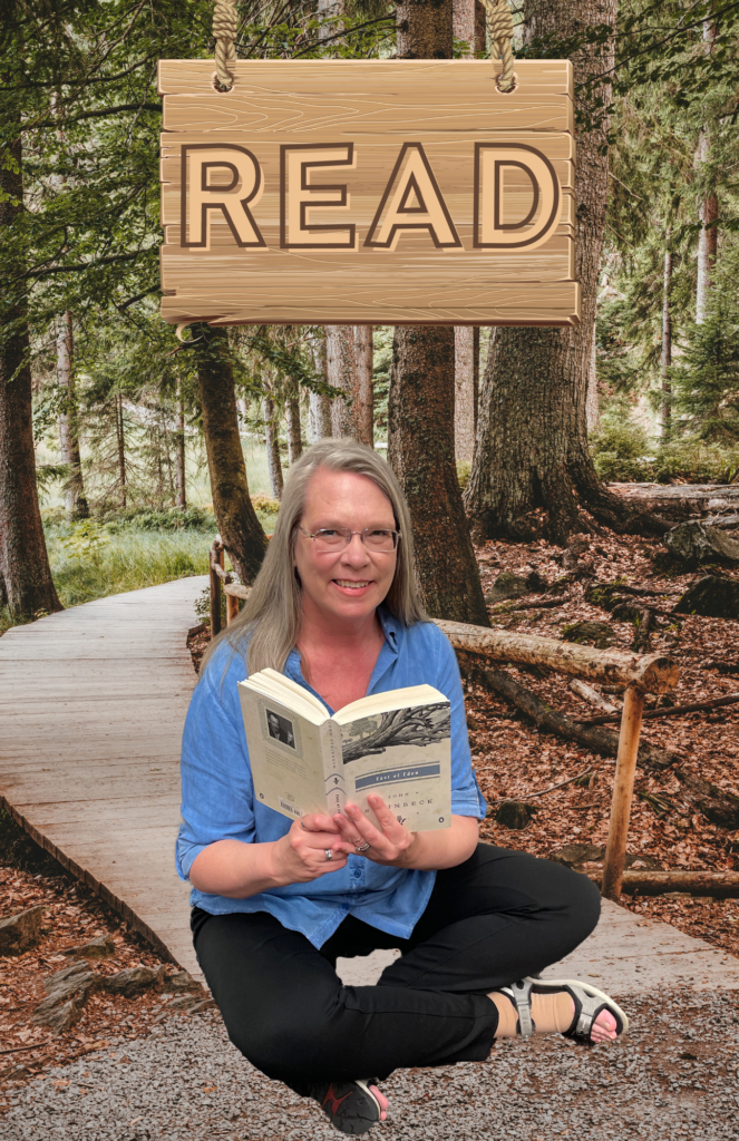 C-SPL June 2023 Reader of the Month.
Woman holding an open book and sitting on the ground in a woodsy environment with a wooden "READ" sign above her head.