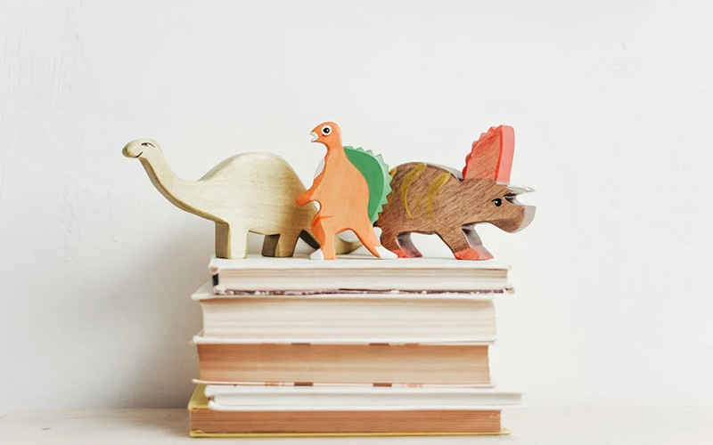 Stack of books with wooden toy dinosaurs on top. Poetry books for storytime.