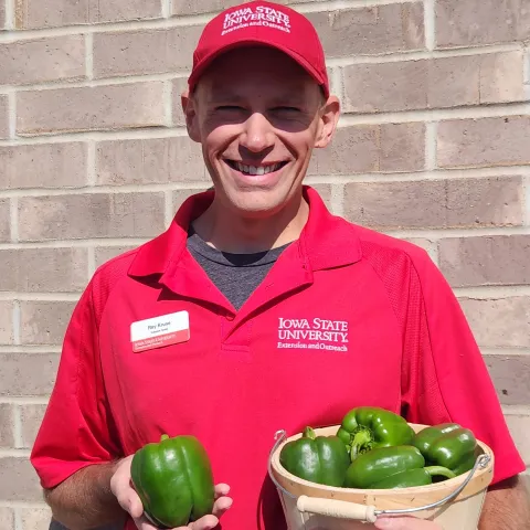 Man wearing red polo and hat holding a bushel of green peppers.